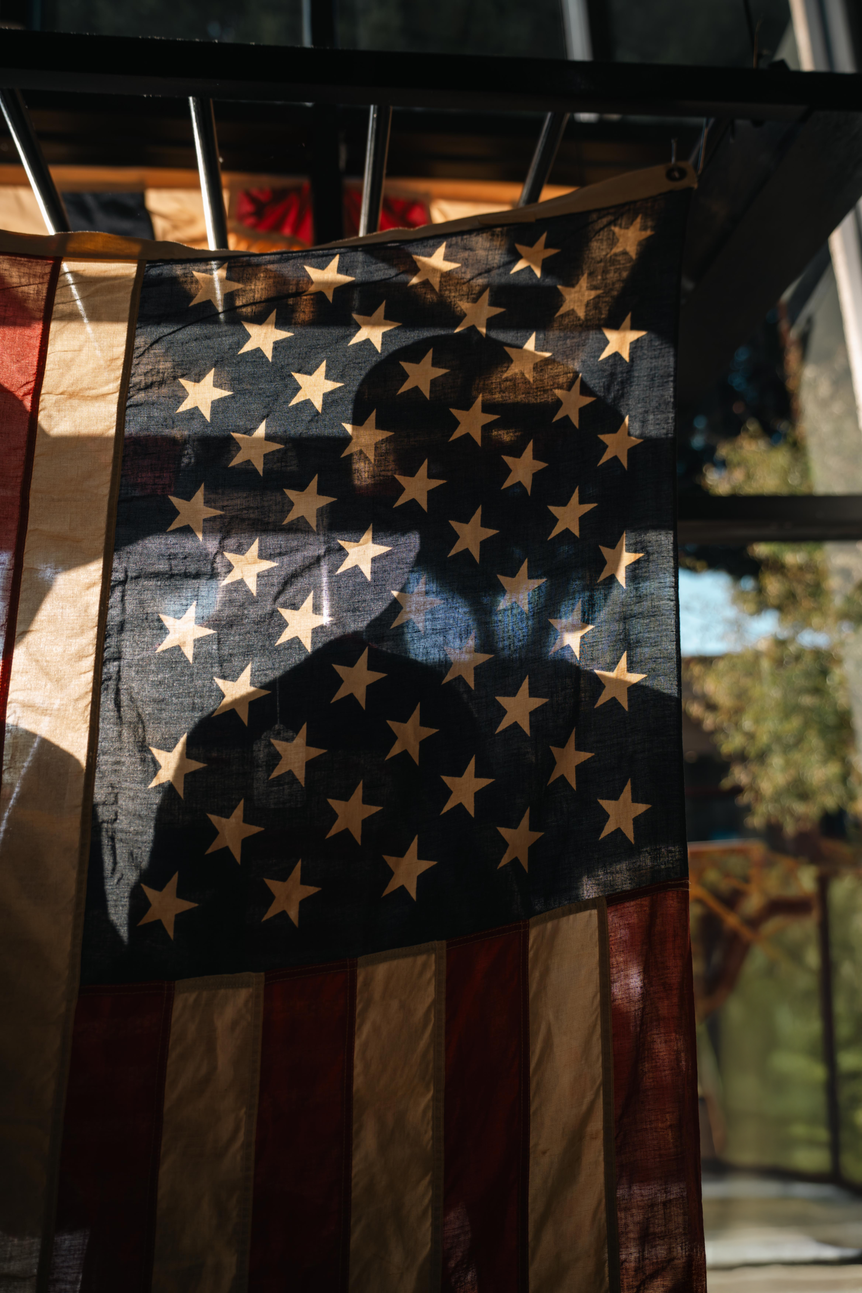 A mysterious silhouette cast on a softly lit American flag indoors.